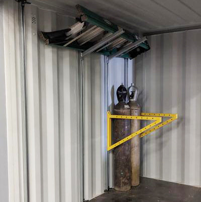 Galvanized steel CSM pipe rack installed inside a shipping container, securely holding gas cylinders with a yellow safety bracket and supporting a ladder on the overhead strut system.