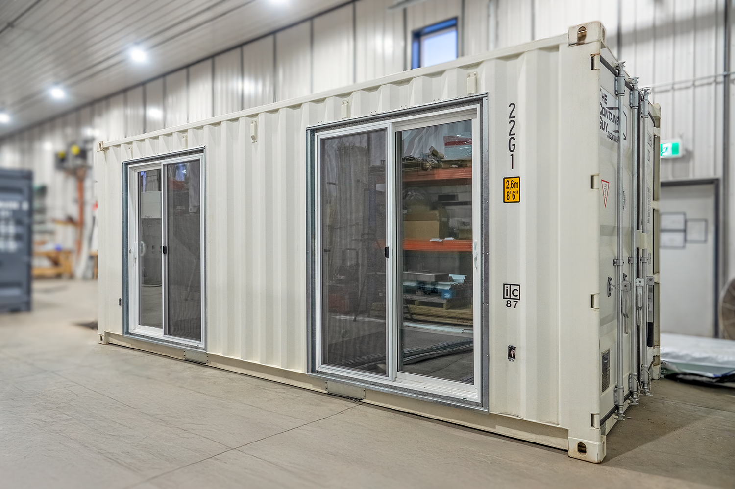 Two galvanized steel sliding patio door frames with doors installed side-by-side on the corrugated sidewall of a shipping container, creating a sleek and modern exterior finish.