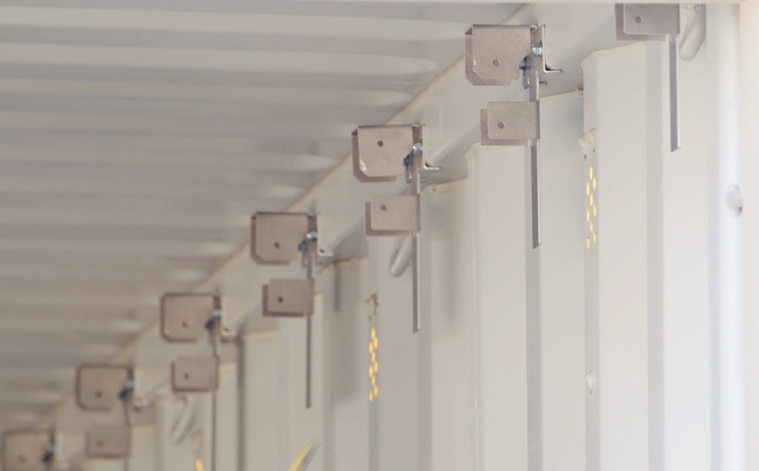 Row of aluminum interior wood stud brackets installed along the top tubing of a white shipping container for framing support