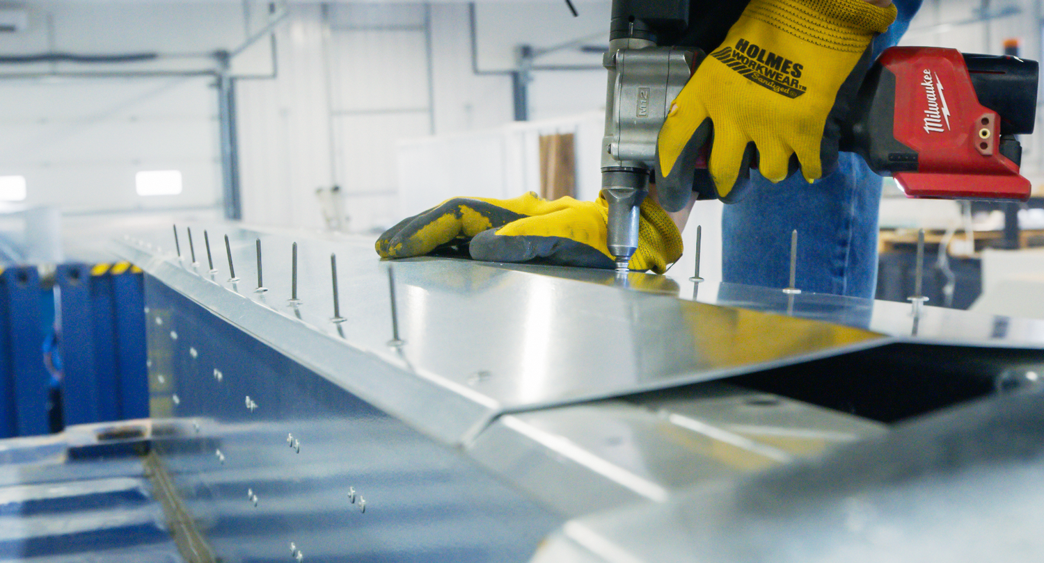 Weldless battery powered rivet gun installing ridge cap between two 40ft shipping containers