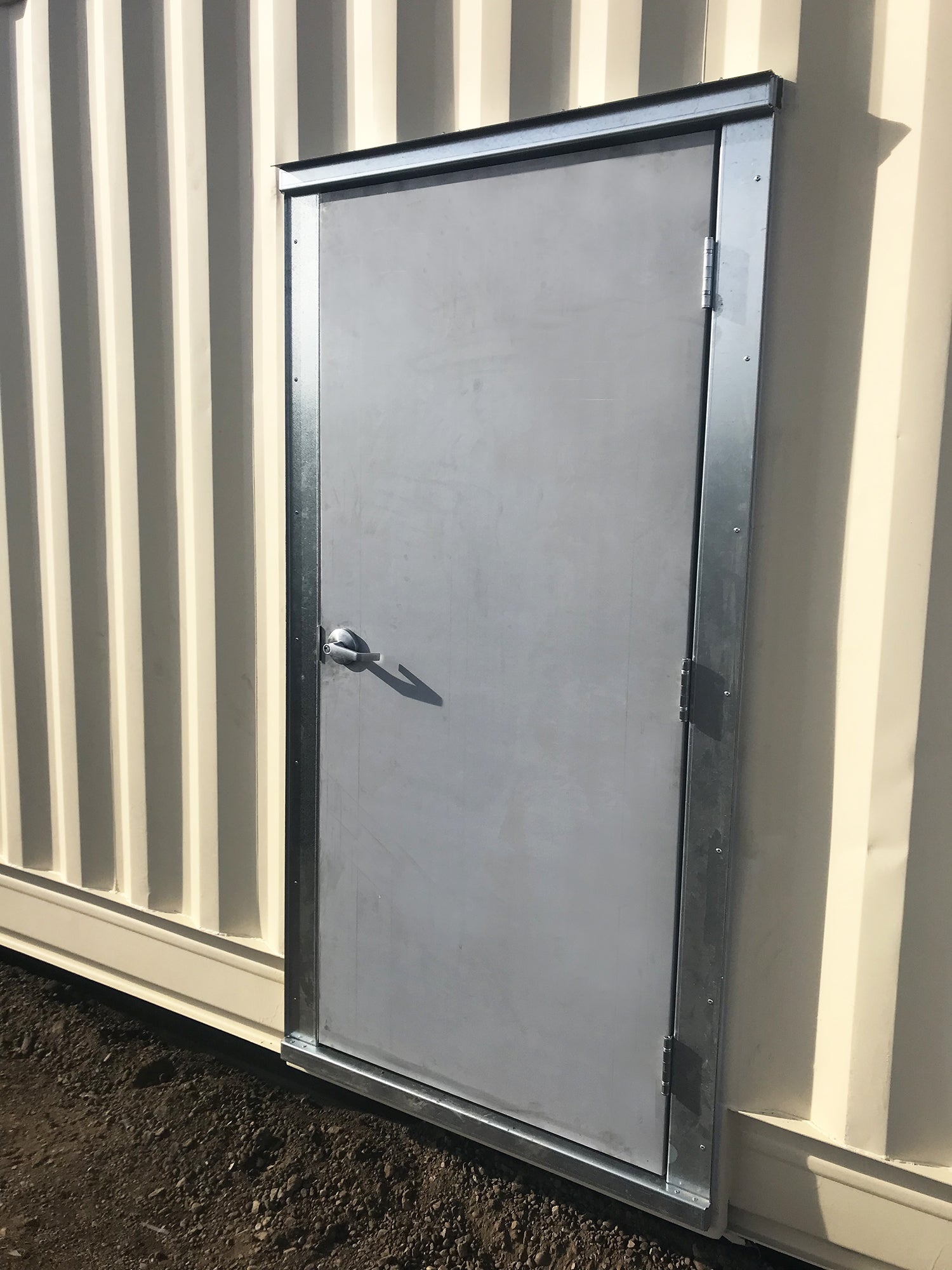 Steel man door with galvanized frame installed on the side of a beige shipping container for secure container access.