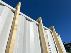 Galvanized steel brackets supporting vertical wood framing on white shipping container exterior