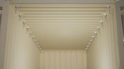 Interior view of a shipping container with aluminum wood stud brackets evenly installed along the top tubing on both walls for framing installation