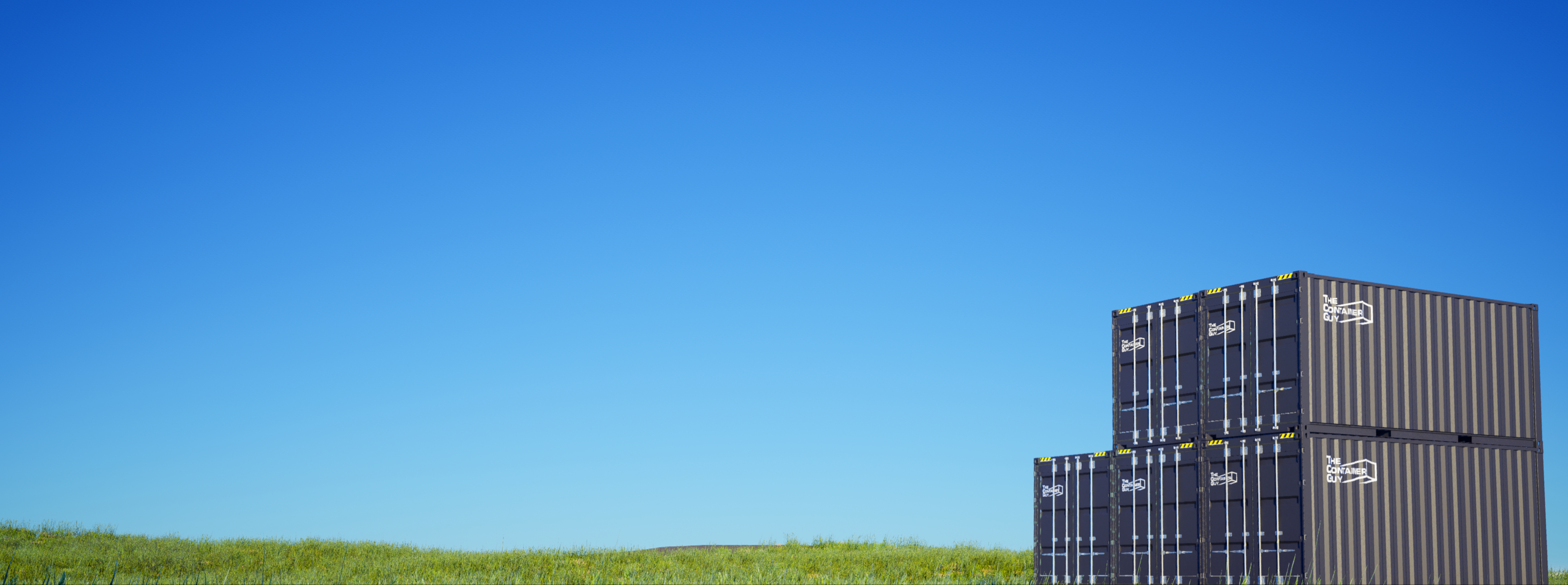 The Container Guy shipping containers stacked beside a grassy field under a blue sky
